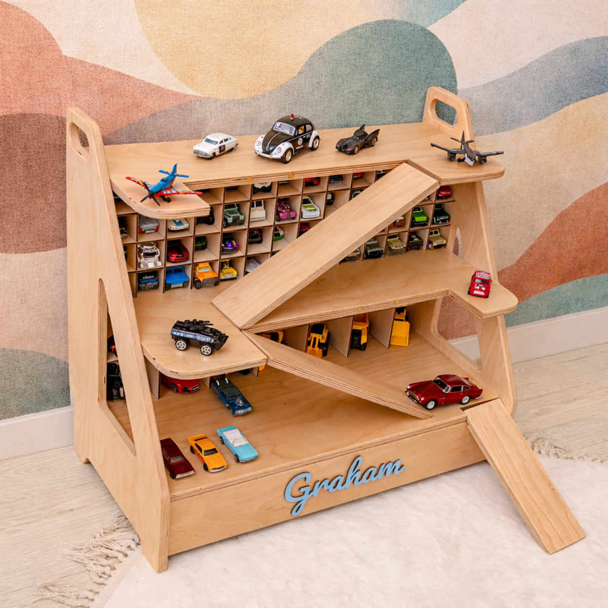 Light wood personalized toy car garage with name Graham in blue 3D letters, filled with toy cars in a kids playroom