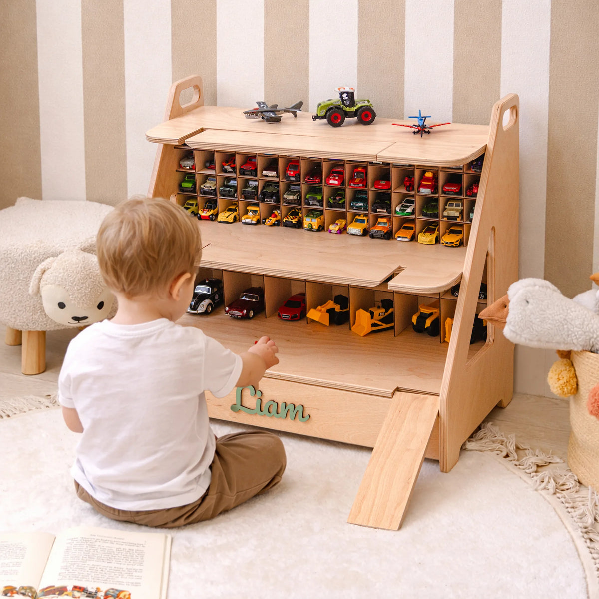Child sitting in front of a wooden toy car garage filled with cars in a striped nursery
