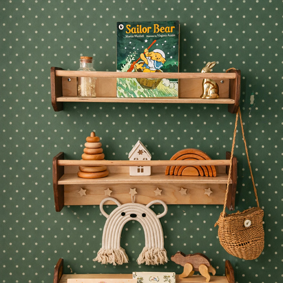 Dark wood Montessori wall shelves with books, toys and a bag hanging on star-shaped wooden pegs