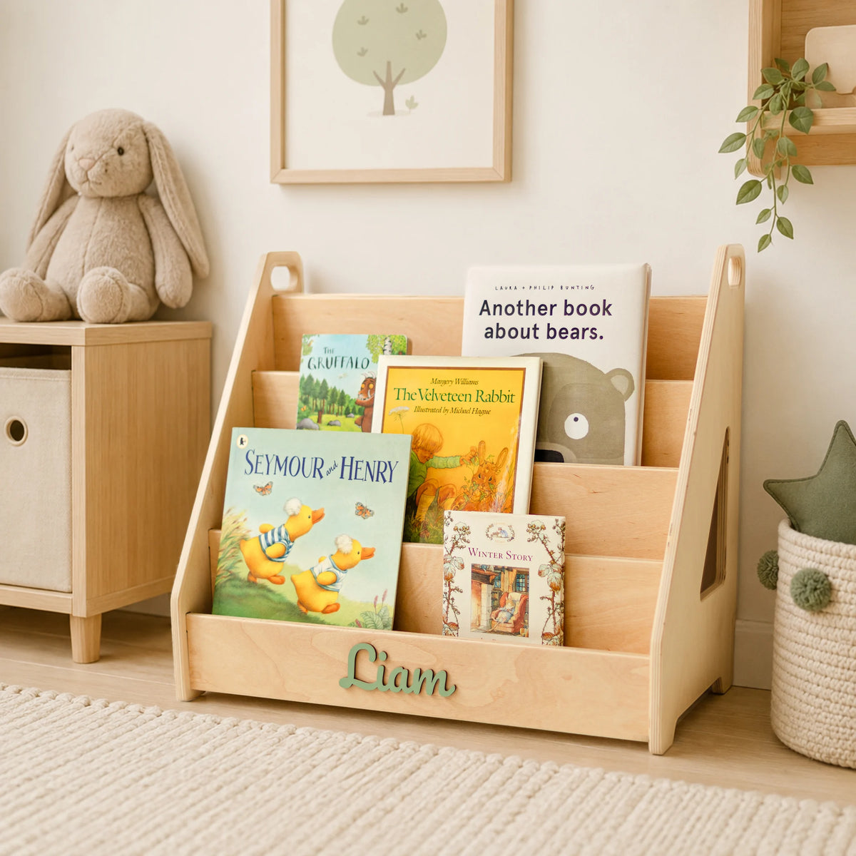 Light wood Montessori bookshelf with name Liam styled in a nursery corner with a teddy bear and cabinet