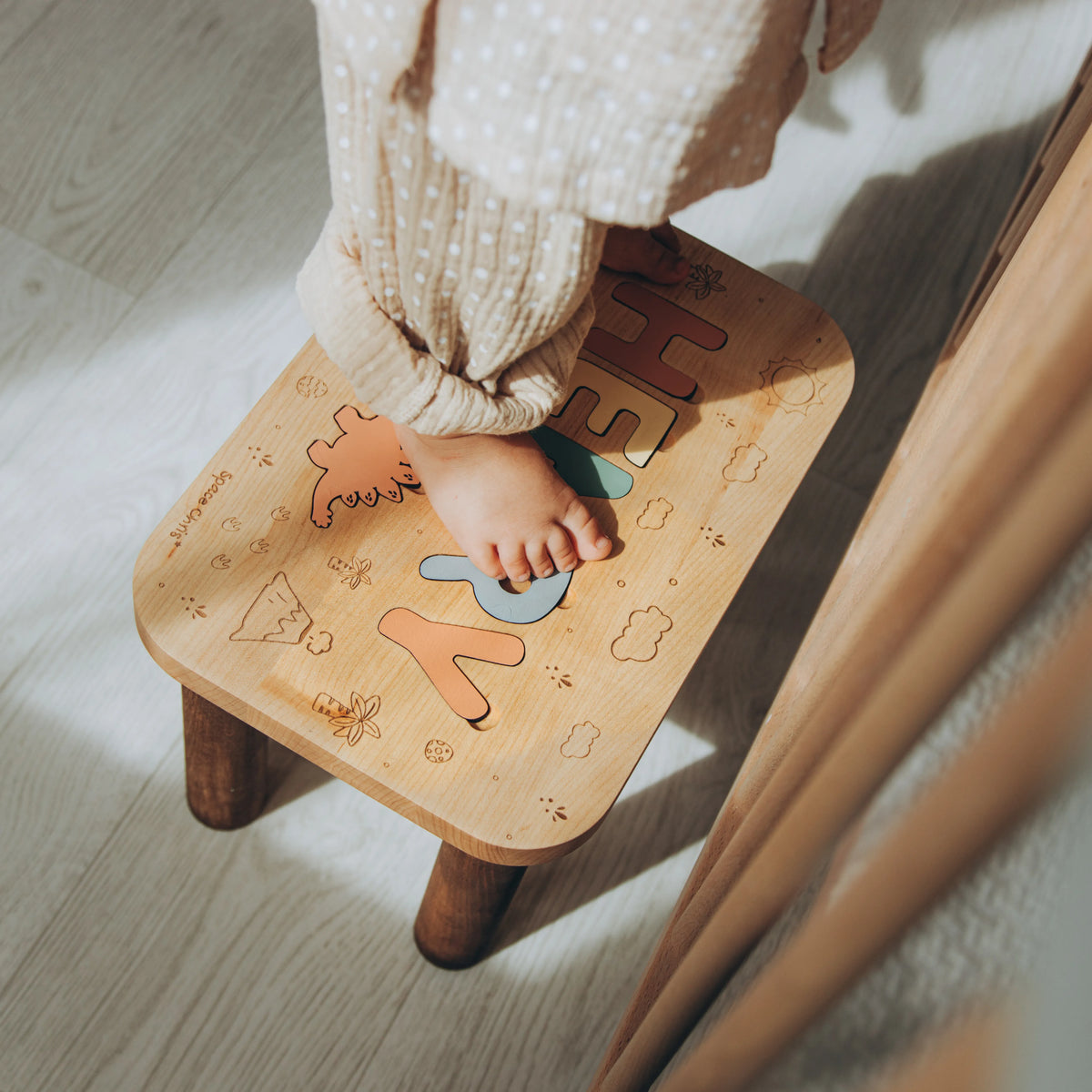 Toddler standing safely on a sturdy personalized wooden step stool with dinosaur engravings.