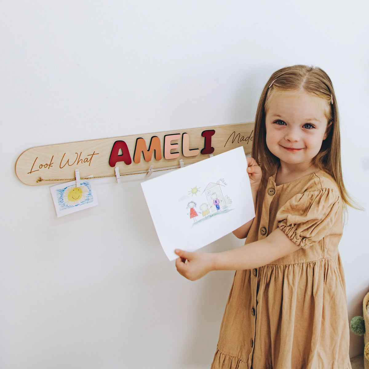 Girl hanging her drawing on a personalized Look What I Made sign with the name Ameli