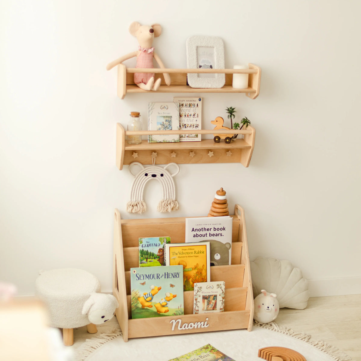 Light wood wall shelf set with front-facing picture books, wooden toys and hanging bag in a nursery