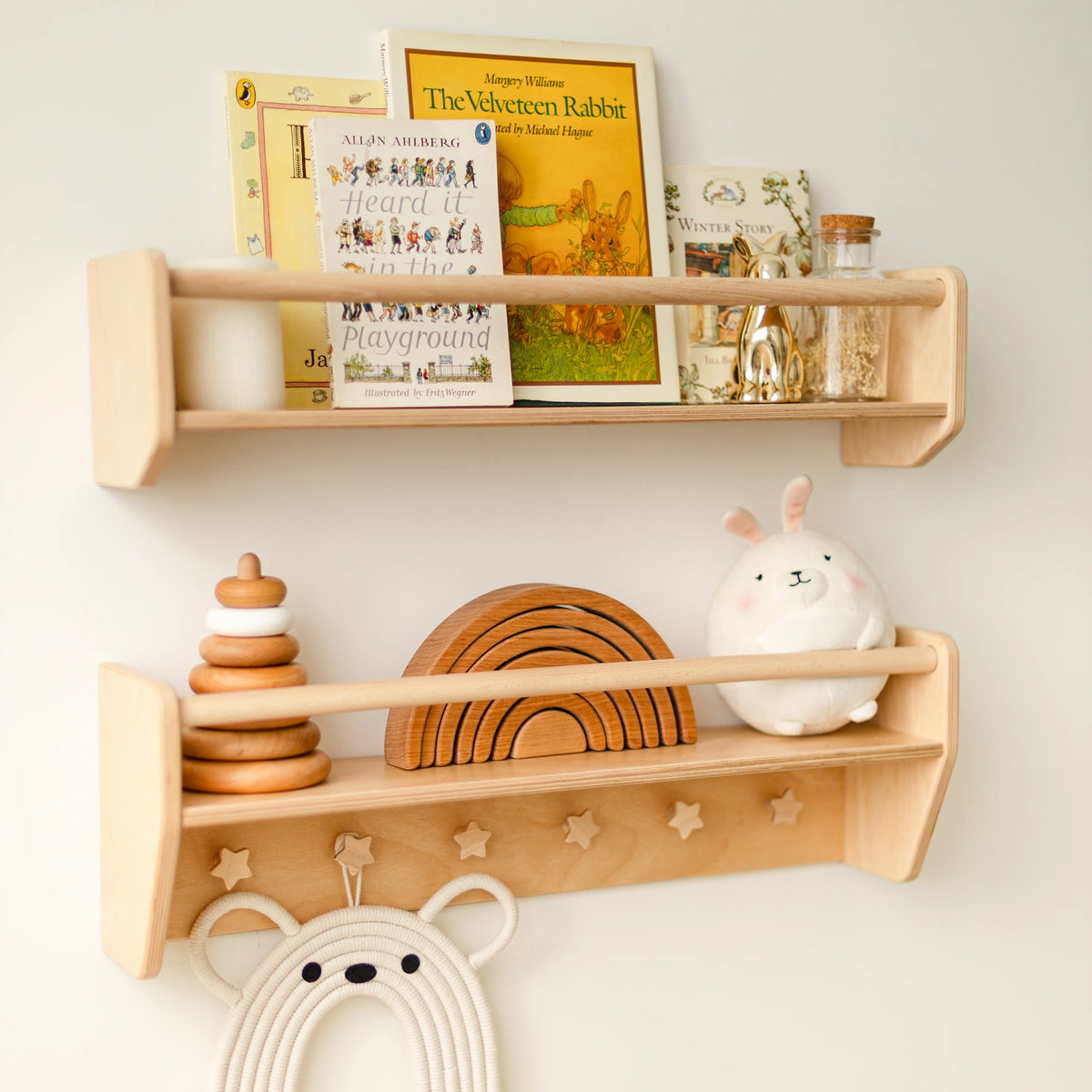 Light wood wall shelf set with books, wooden rainbow and macrame bear on a white nursery wall