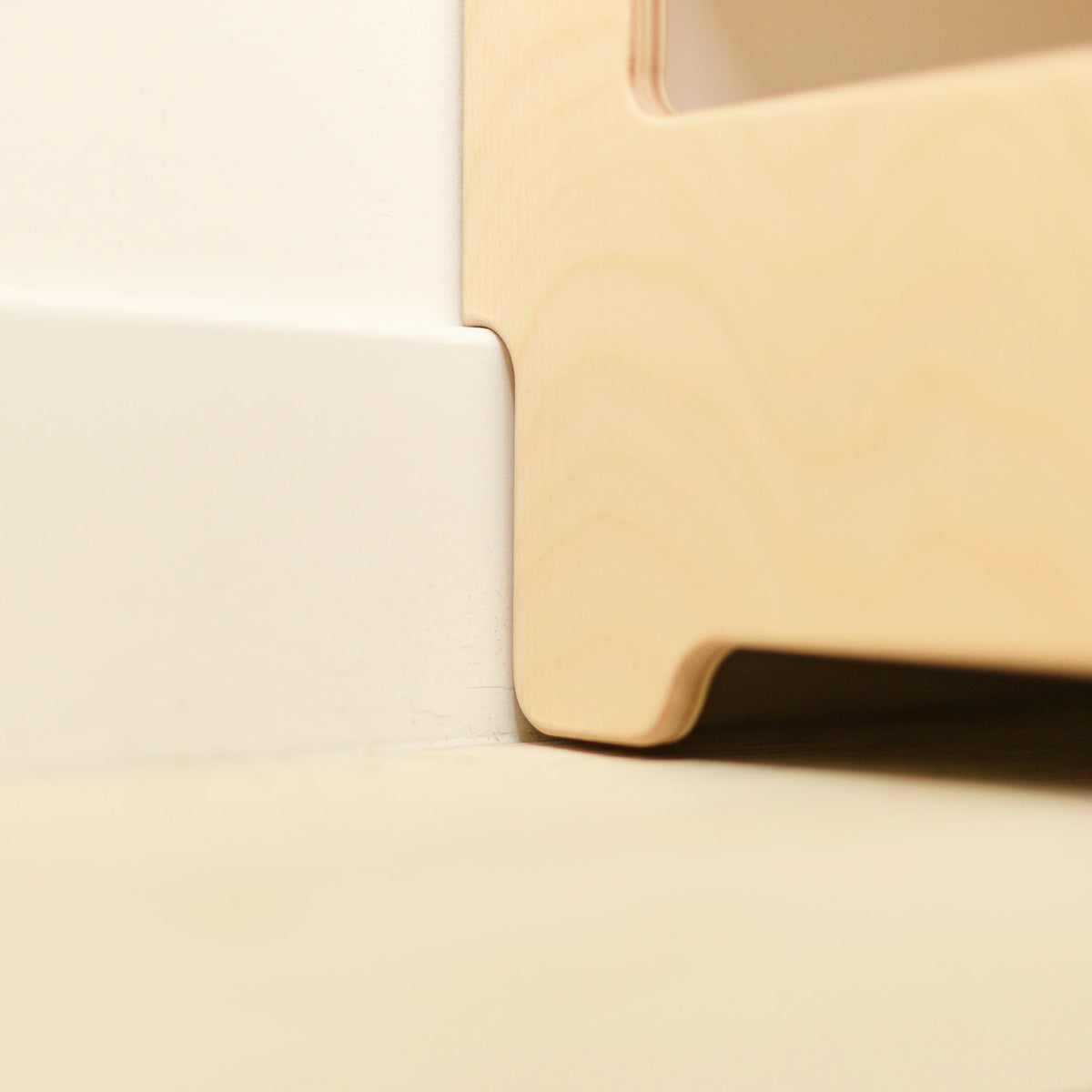 Close-up of the smooth rounded edge of a wooden Montessori bookshelf, showing the child-safe finish