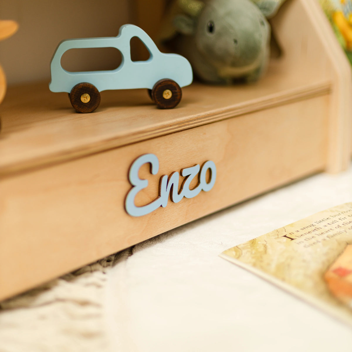 Close-up of a light wood shelf with a wooden blue toy car and the name Enzo in blue 3D letters