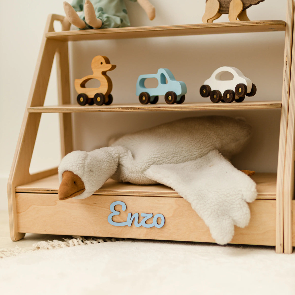Close-up of a light wood Montessori toy shelf topped with wooden toy cars, name Enzo in green 3D letters