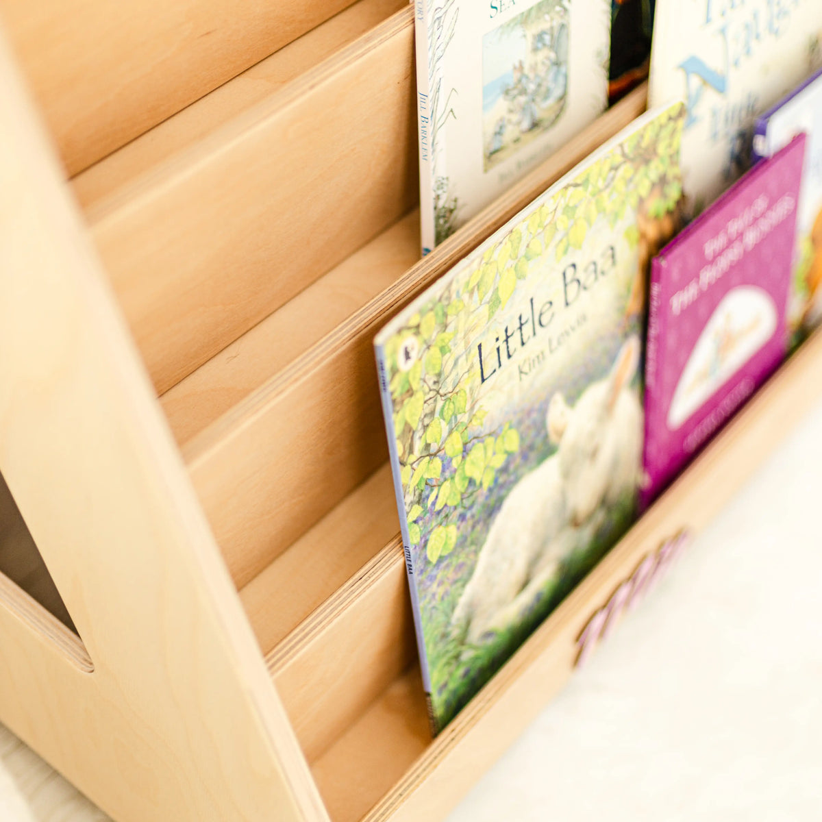 Close-up of a light wood front-facing bookshelf holding picture books on tiered display shelves