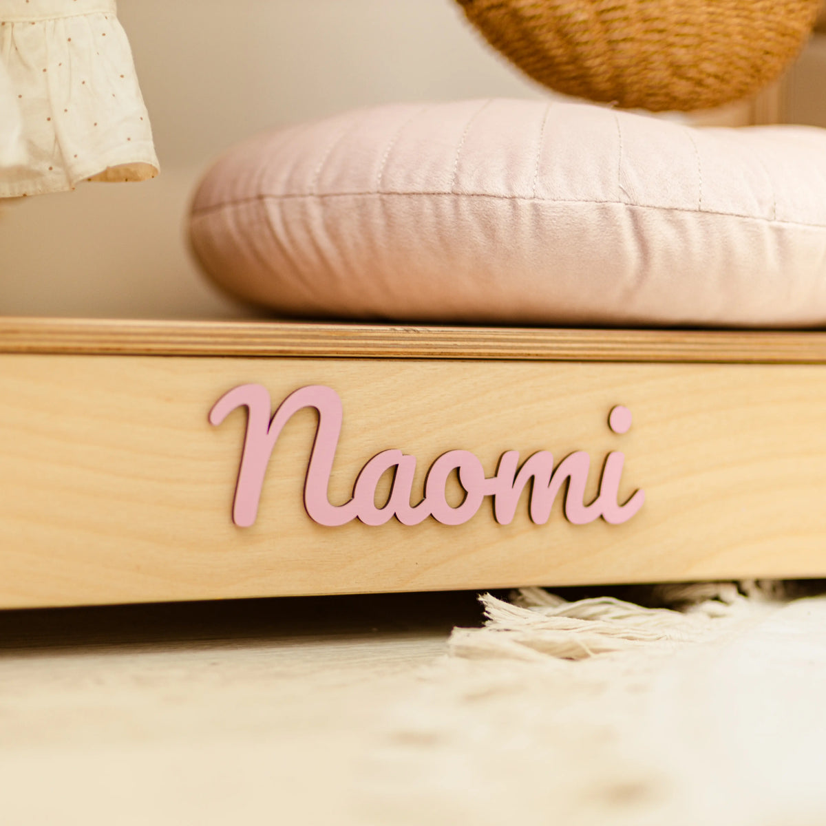 Close-up of the name Naomi in pink 3D wooden letters on the base of a light wood clothing rack