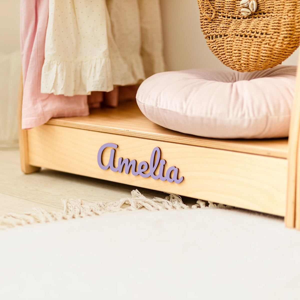Close-up of the name Amelia in purple 3D wooden letters on a light wood clothes rack