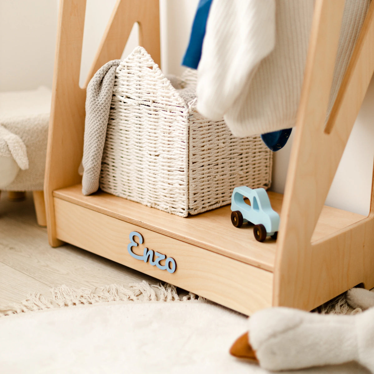 Light wood clothing rack base with a woven storage basket and a wooden toy car, name Enzo