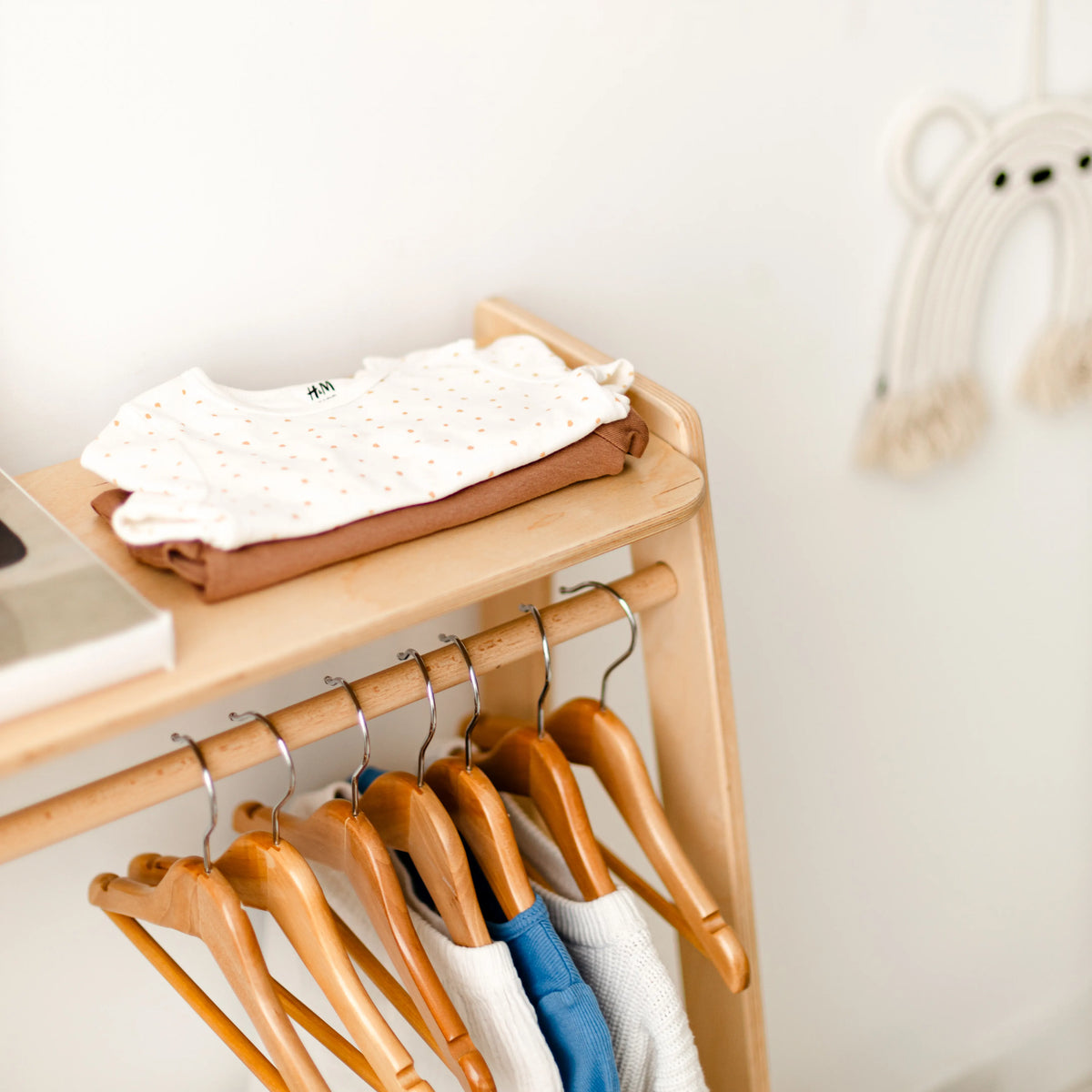 Close-up of a kids' clothing rack rail with clothes on wooden hangers and a folded item on the shelf