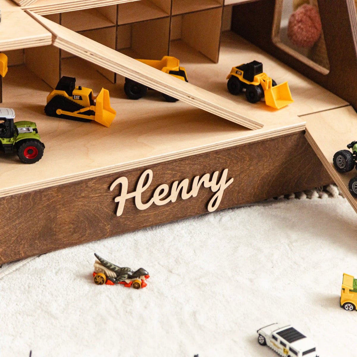 Close-up of a dark wood toy car garage ramp with the name Henry in raised wooden letters