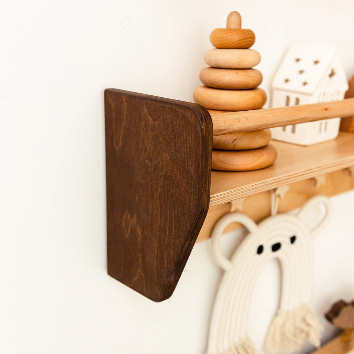 Dark wood Montessori wall shelf with star-shaped wooden pegs and a stacking ring toy on a white wall