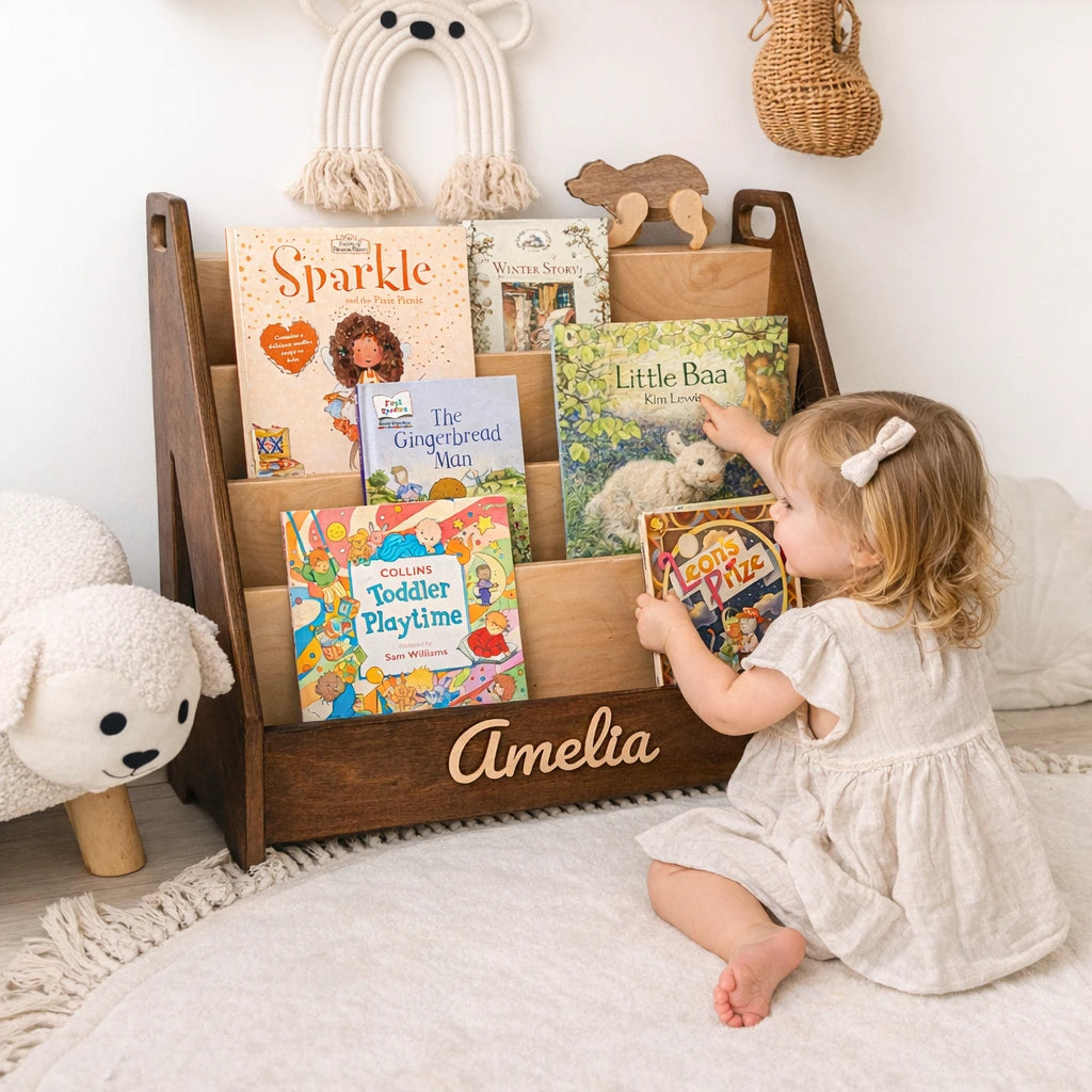 Dark wood personalized Montessori bookshelf with name Amelia, toddler girl choosing a front-facing book in a nursery