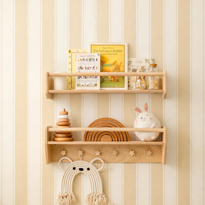 Light wood Montessori wall shelf set with star cut-outs, holding books, wooden toys and a macrame bear in a nursery