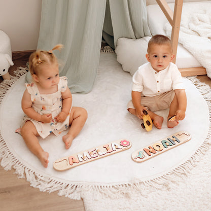 Two toddlers playing with name puzzles spelling Amelia and Noah on a round rug