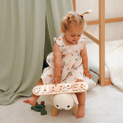 Toddler playing with a wooden name puzzle spelling Harper on the floor