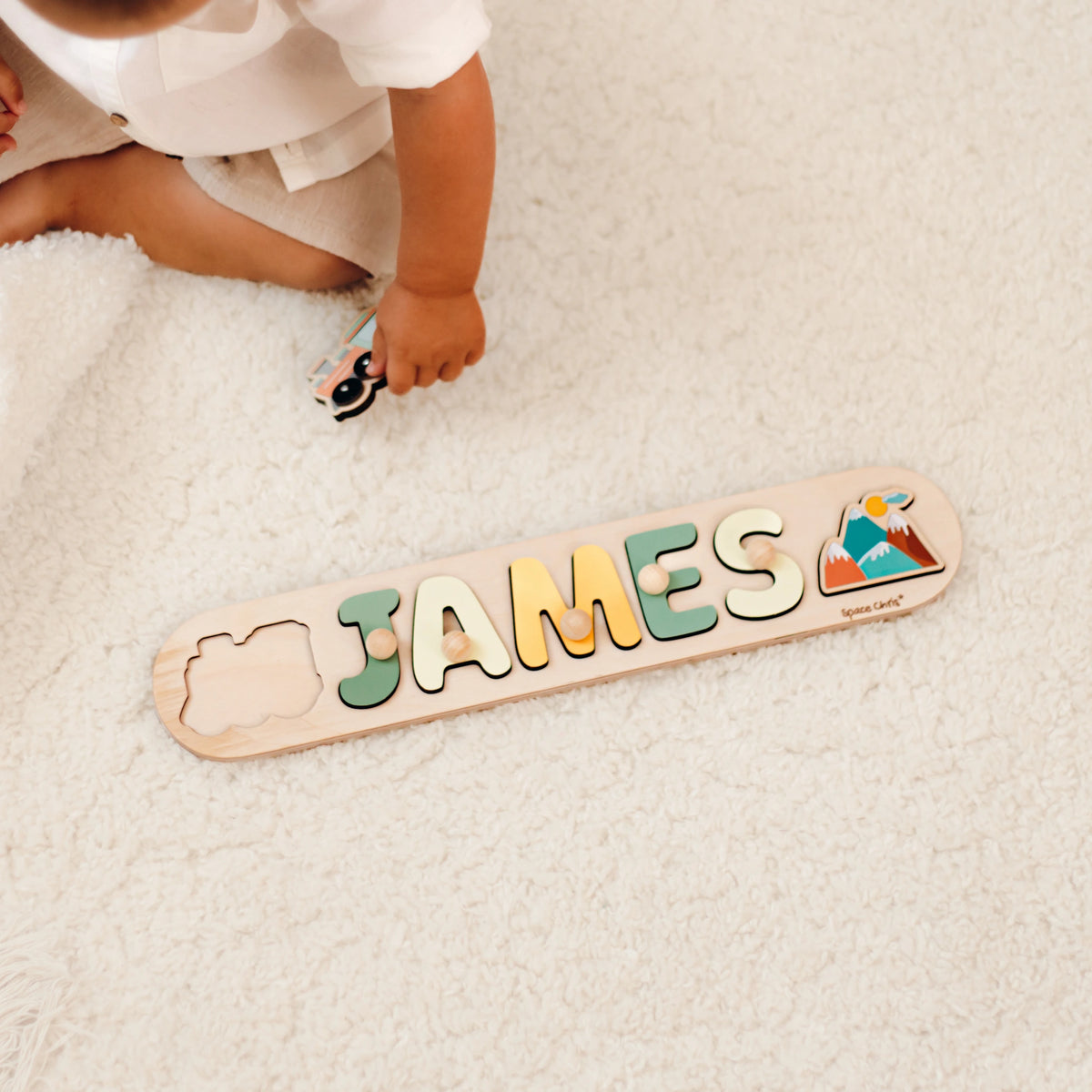 Baby playing with a wooden name puzzle spelling James with a dolphin piece