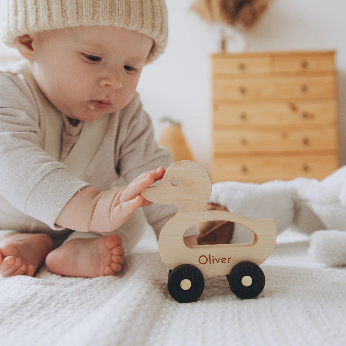 Baby reaching for personalized yellow wooden duck toy on wheels