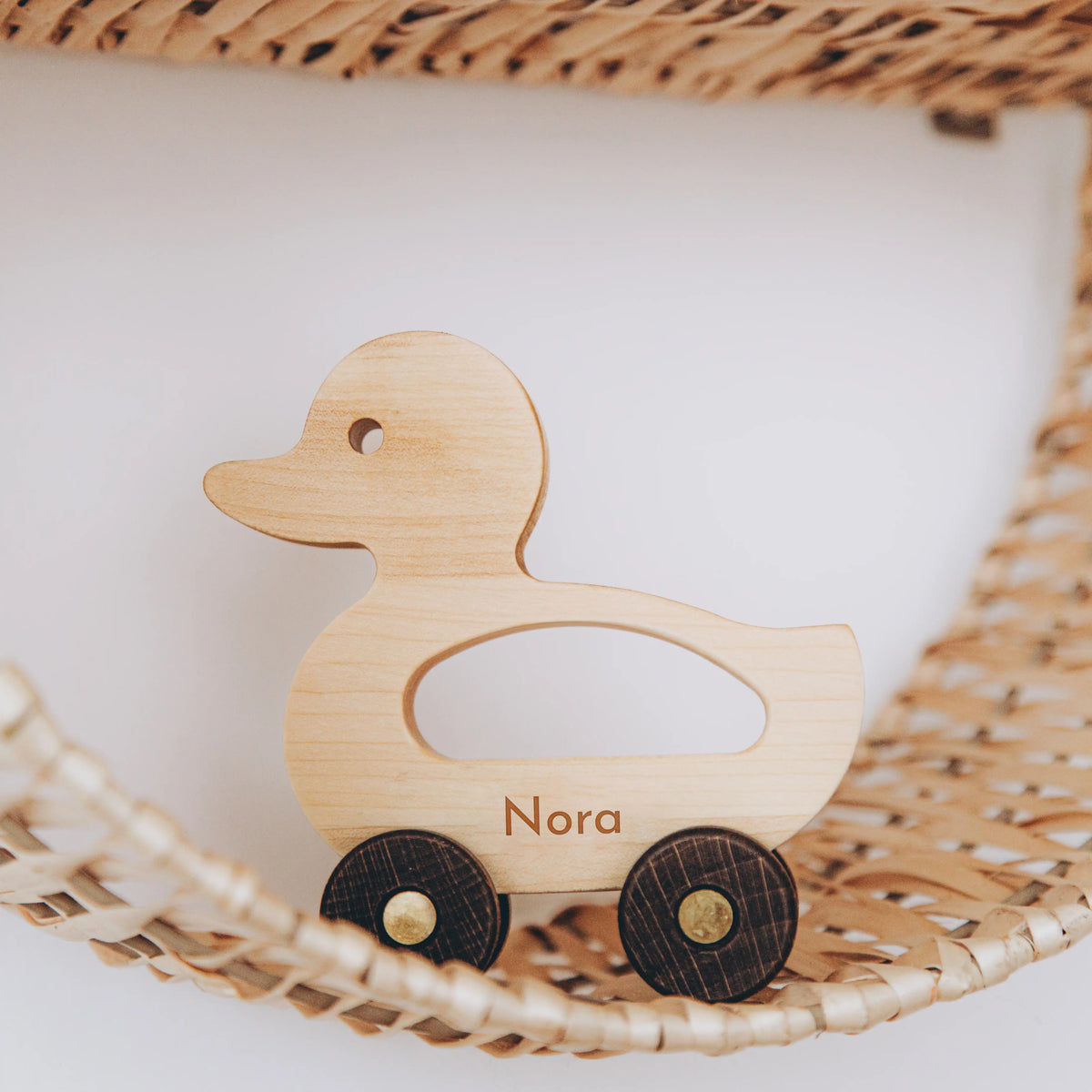 Personalized light wood duck toy with name Nora on wicker basket