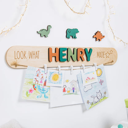 Wooden Look What I Made art display with the name Henry in green letters, holding children's drawings with clips and dinosaur pieces