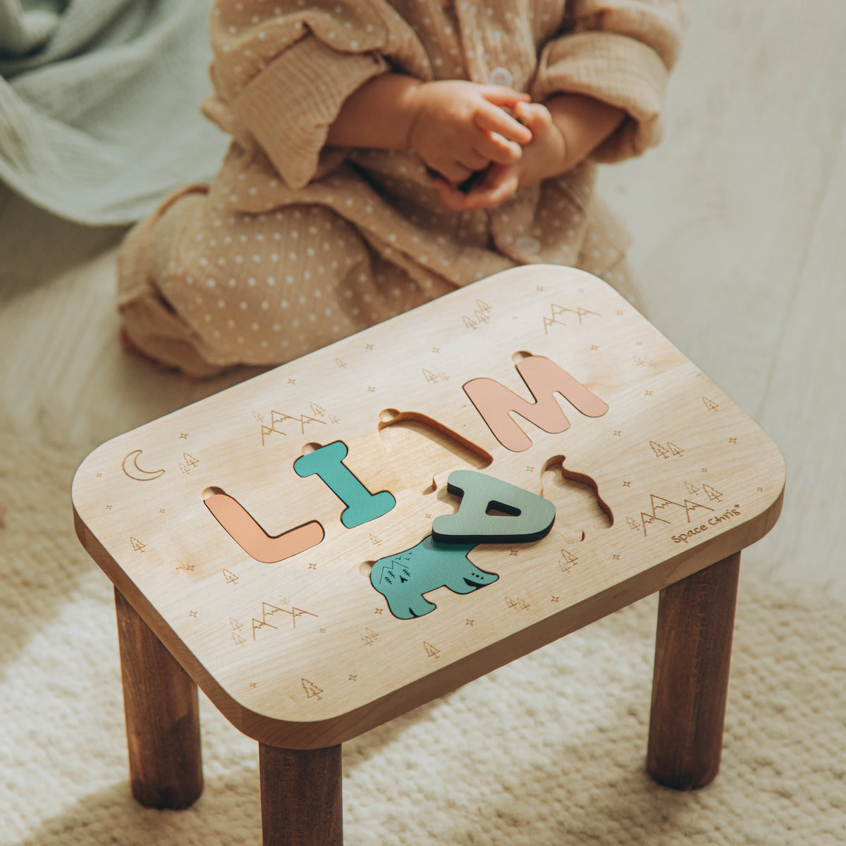 Child playing with the name Liam on a custom wooden puzzle step stool with forest animal cutouts.