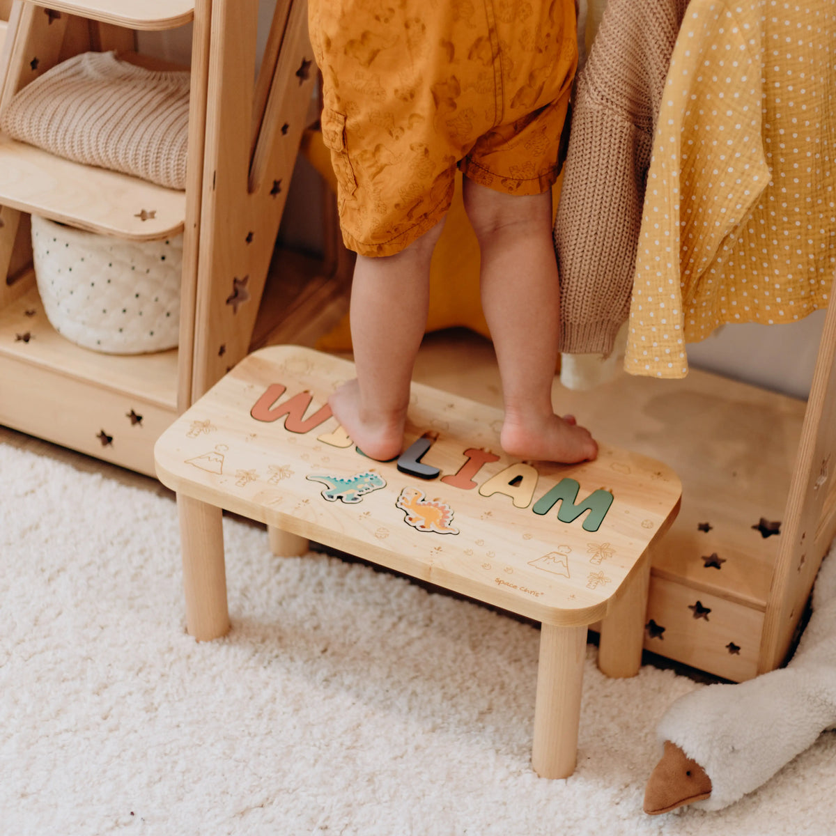 Toddler safely standing on a sturdy personalized wooden step stool to reach a higher shelf.