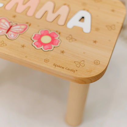 Close up of printed butterfly and flower puzzle pieces on a personalized wooden name stool for girls.