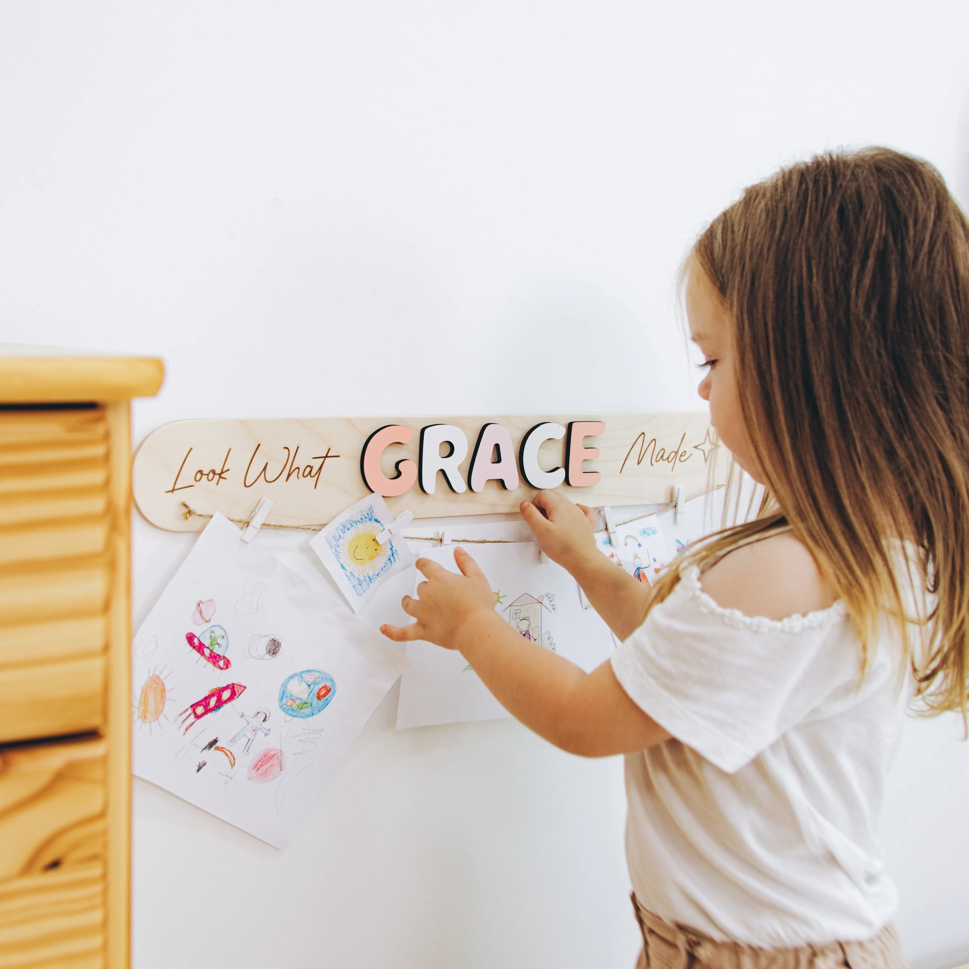 Girl hanging her drawing on a personalized Look What I Made sign with the name Grace