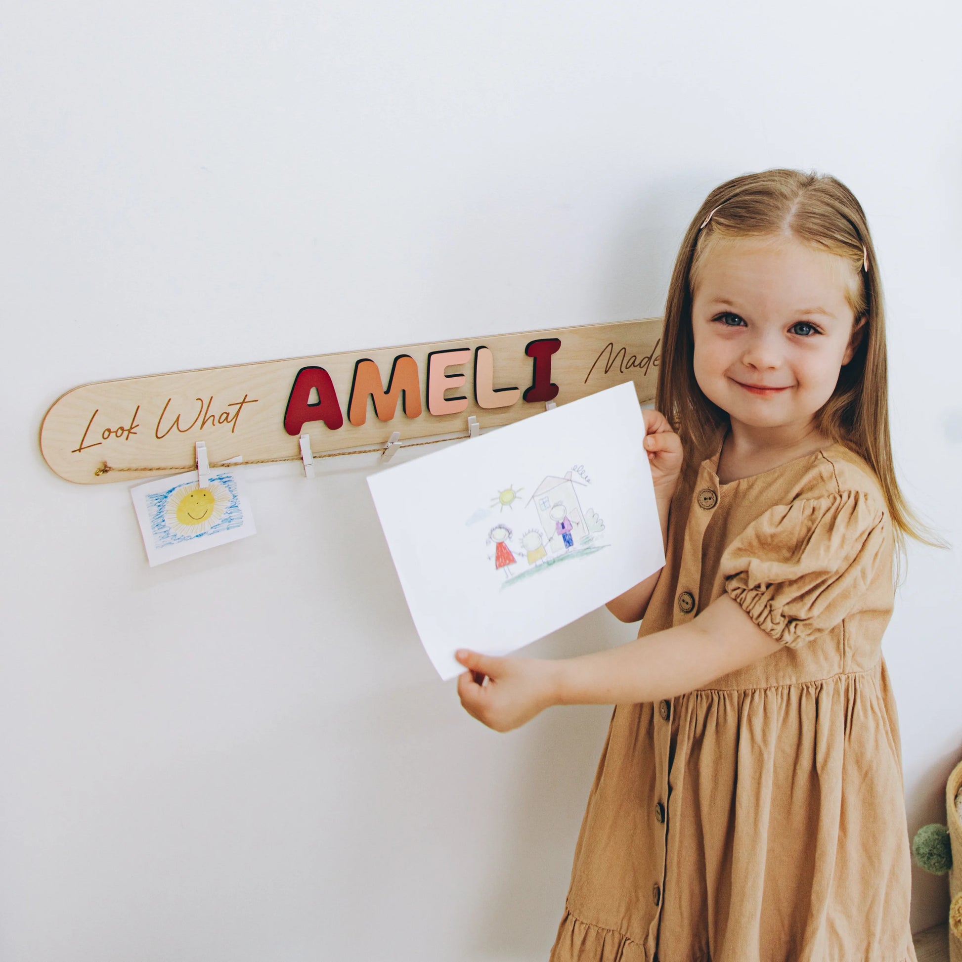 Girl hanging her drawing on a personalized Look What I Made sign with the name Ameli