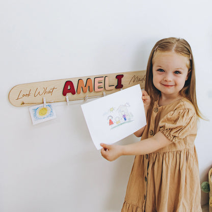 Girl hanging her drawing on a personalized Look What I Made sign with the name Ameli