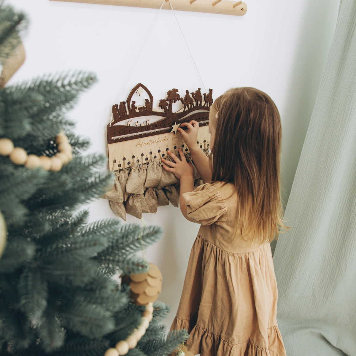 Little girl decorating a Christmas tree with a wooden Nativity advent calendar
