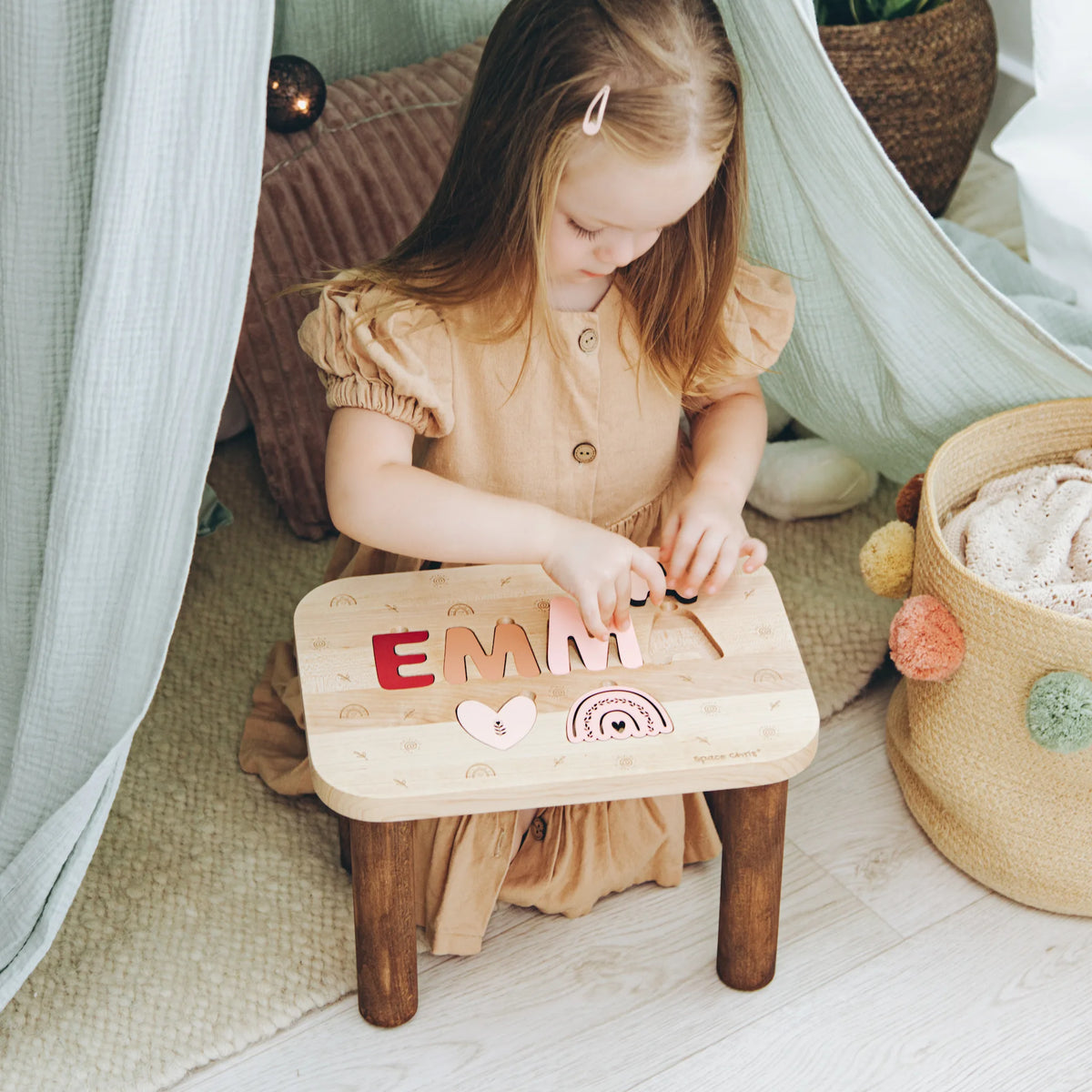 Toddler girl sitting in a teepee playing with her personalized Boho theme wooden name puzzle stool.