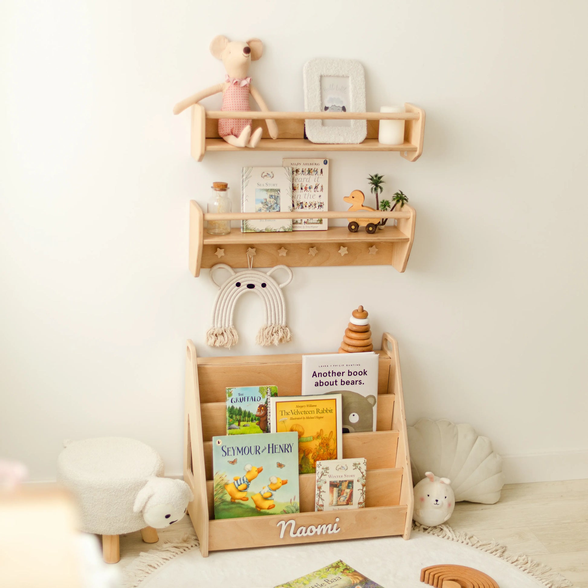 Light wood wall shelf set with front-facing picture books, wooden toys and hanging bag in a nursery