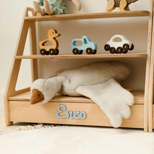 Close-up of a light wood Montessori toy shelf topped with wooden toy cars, name Enzo in green 3D letters