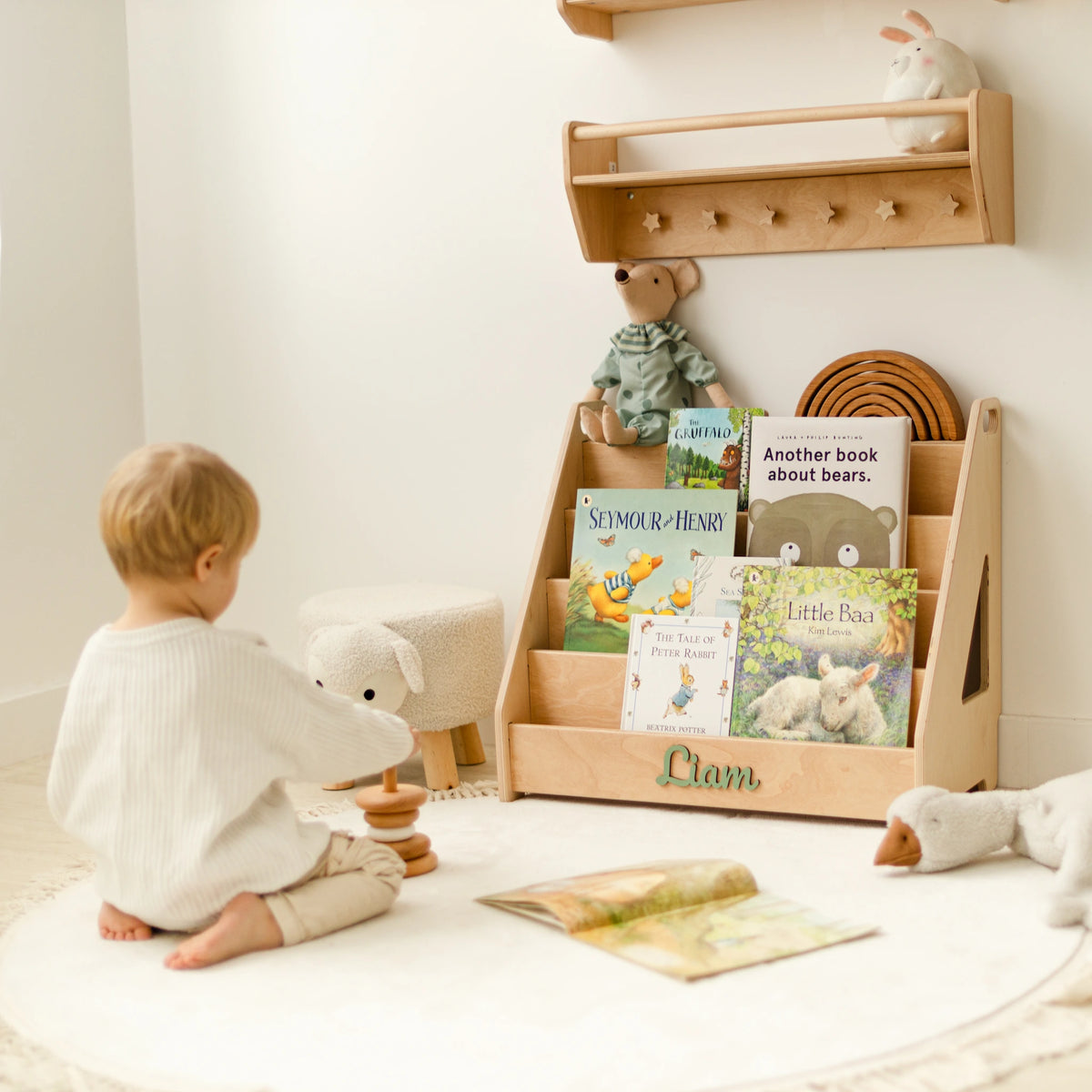 Toddler playing in front of a light wood front-facing Montessori bookshelf with 3D name