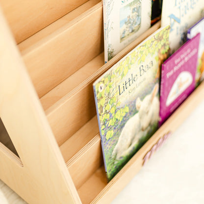 Close-up of a light wood front-facing bookshelf holding picture books on tiered display shelves