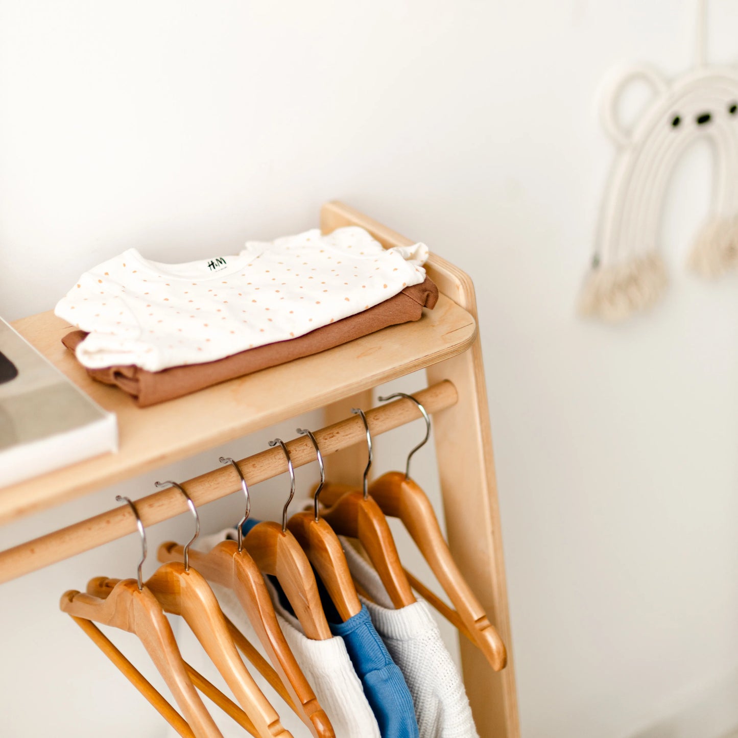 Close-up of a kids' clothing rack rail with clothes on wooden hangers and a folded item on the shelf