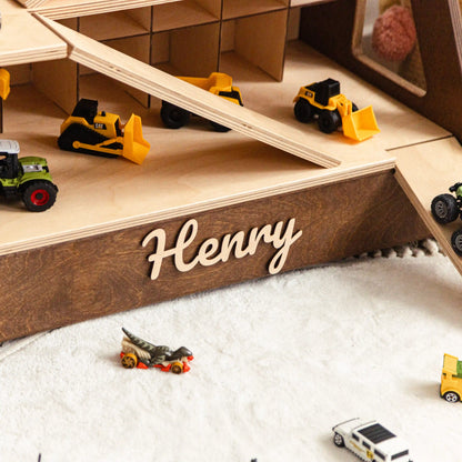 Close-up of a dark wood toy car garage ramp with the name Henry in raised wooden letters