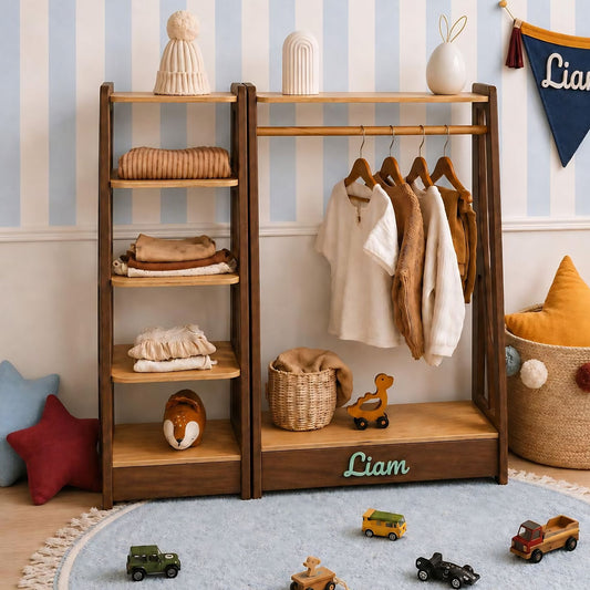 A wooden children's clothing rack with shelves and hanging rods, styled in a nursery with toys, pillows, and striped wallpaper. The rack is personalized with the name 'Liam' on the bottom shelf.